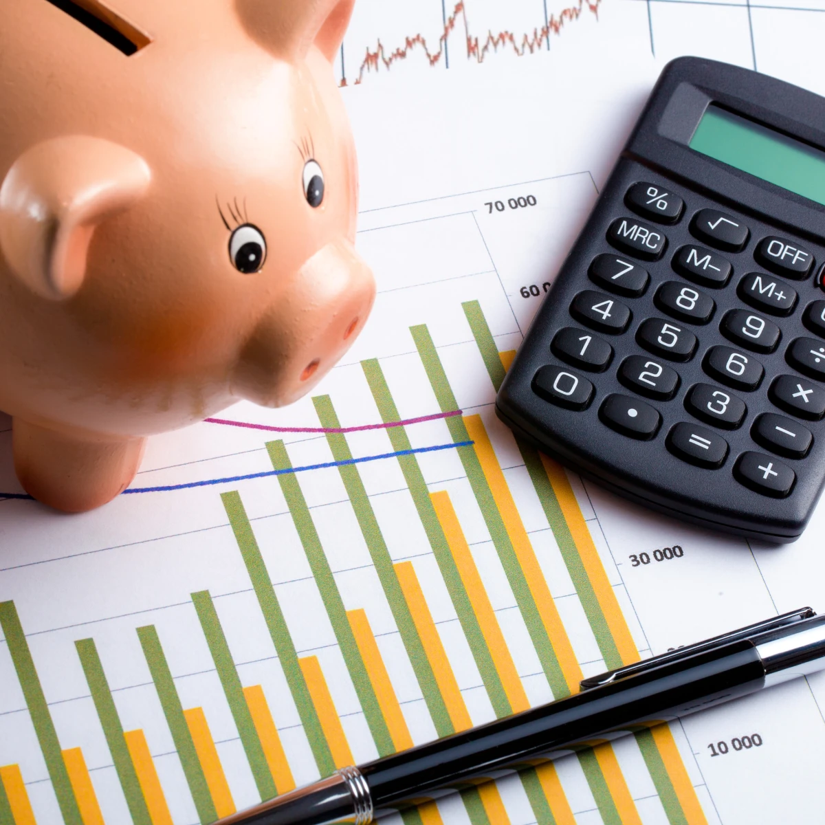 돼지 저금통과 계산기, 그리고 상승과 하락이 교차하는 성과 그래프가 그려진 서류 위에 놓인 펜, 병원 마케팅 비용 효율을 분석하는 이미지