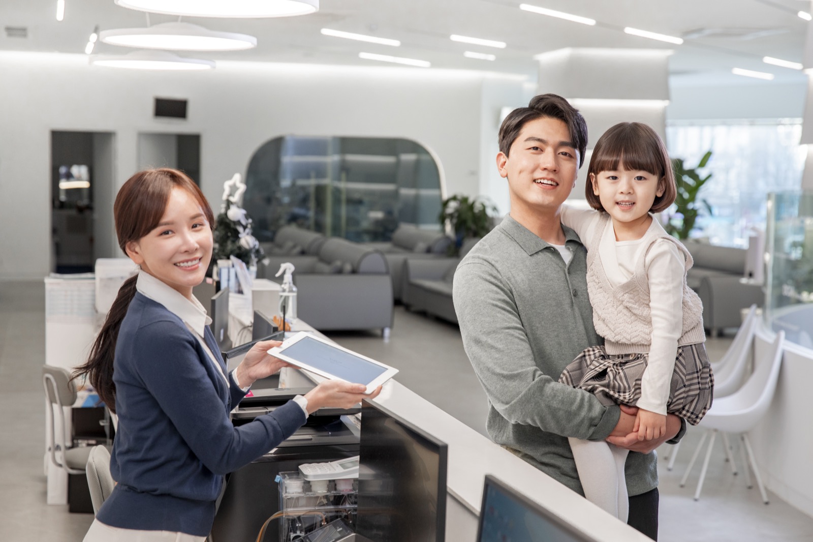 병원 접수데스크에서 직원이 아이를 안은 보호자를 응대하는 모습